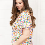 Woman with dark hair standing in a side profile position wearing the Basic Tee against a white background. The focal point of this image is the color otomi pattern. The model paired this top with dark-wash denim shorts. 