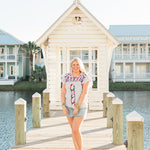 Woman with blonde hair standing in a front profile position wearing the Beck Top in a lifestyle scene. The focal point of this image is the top in its entirety. The model paired this top with a light-wash denim skirt. 