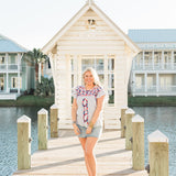 Woman with blonde hair standing in a front profile position wearing the Beck Top in a lifestyle scene. The focal point of this image is the top in its entirety. The model paired this top with a light-wash denim skirt. 
