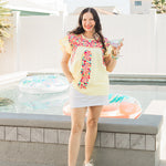 Woman with dark hair standing in a front profile position wearing the Beck Top in a lifestyle scene. The focal point of this top is the top in its entirety. The model paired this top with a white skirt and silver sneakers.