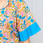Woman with dark hair standing in a front profile position wearing the Bell Top against a white background. This up-close image allows you to see better graphic detail as well as the ruffled sleeves and tassels on front of the top.