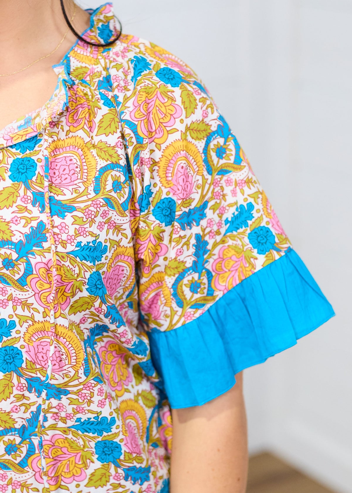 Woman with dark hair standing in a front profile position wearing the Bell Top against a white background. This up-close image allows you to see better graphic detail as well as the ruffled sleeves and tassels on front of the top.