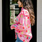 Woman with dark hair wearing a multi-color Christmas tree graphic long-sleeve with ruffles on sleeves. Model paired this top with dark-wash denim jeans. 