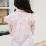 Woman with dark hair standing in a back profile position wearing the Bridget Top against a white background. the focal point of this image is the pink western toile graphics with ruffles on sleeve. The model paired this top with light-wash denim jeans. 