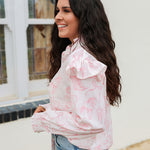 Woman with dark hair standing in a side profile position wearing the Bridget Top against a white background. The focal point of this image is the western toile graphics and ruffles on sleeve. The model paired this top with light-wash denim jeans. 