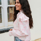 Woman with dark hair standing in a side profile position wearing the Bridget Top against a white background. The focal point of this image is the western toile graphics and ruffles on sleeve. The model paired this top with light-wash denim jeans. 