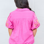 Woman with dark hair standing against a white background wearing the Brinley top. The model is in a back profile position, and paired top with light-wash jeans. 