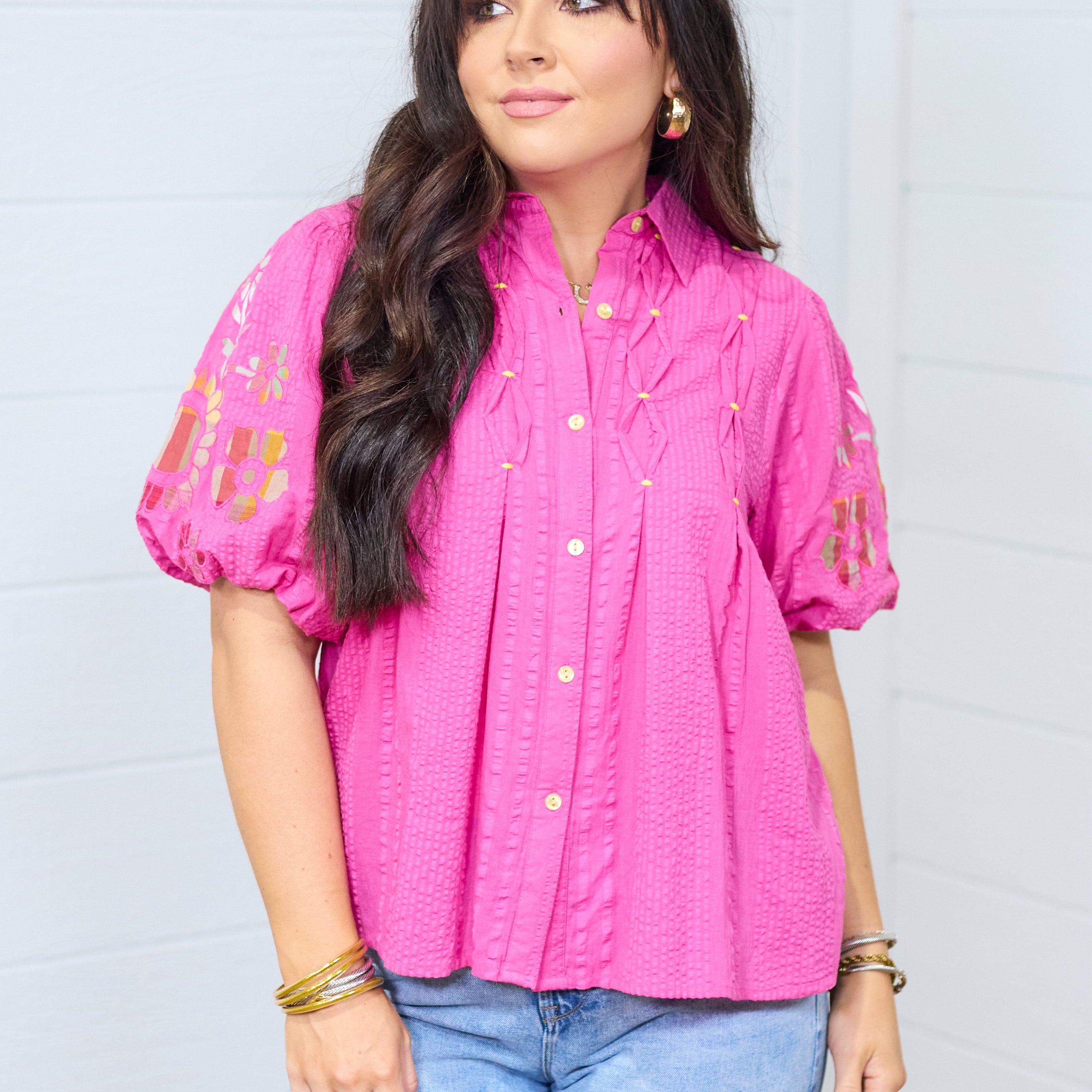 Woman with dark hair wearing the Brinley Top in a front profile position against a white background. The emphasis of this image is the tops front details and embroidery on the front of the sleeves. She paired this top with light-wash denim jeans.