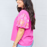 Woman with dark hair standing in a side profile position against a white background. The emphasis of this image is a full length shot of the side of top and showing models light-wash denim jeans. 