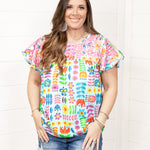 Woman with dark hair standing in a front profile position wearing the Butterfly Top against a white background. The focal point of this image is the top in its entirety. The model paired this top with dark-wash denim shorts. 