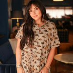 Woman with dark hair standing in a front profile position wearing the Calamity Top in a lifestyle scene. The focal point of this top is the cowboy hat graphics along with buttons down the front. The model paired this top with matching graphic pants. 