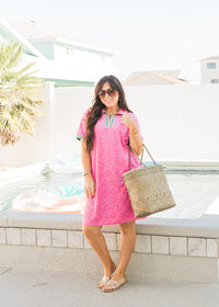 Woman with dark hair standing in front profile position wearing the Cami Dress in a lifestyle scene. The focal point of this image is the dress in its entirety. The model paired this dress with a woven beach bag and transparent sandals with rhinestones. 