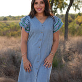 Woman with dark hair standing in a front profile position wearing the Caylee Dress in a lifestyle scene. The focal point of this image is the buttons down the front of dress as well as a v-neckline. 