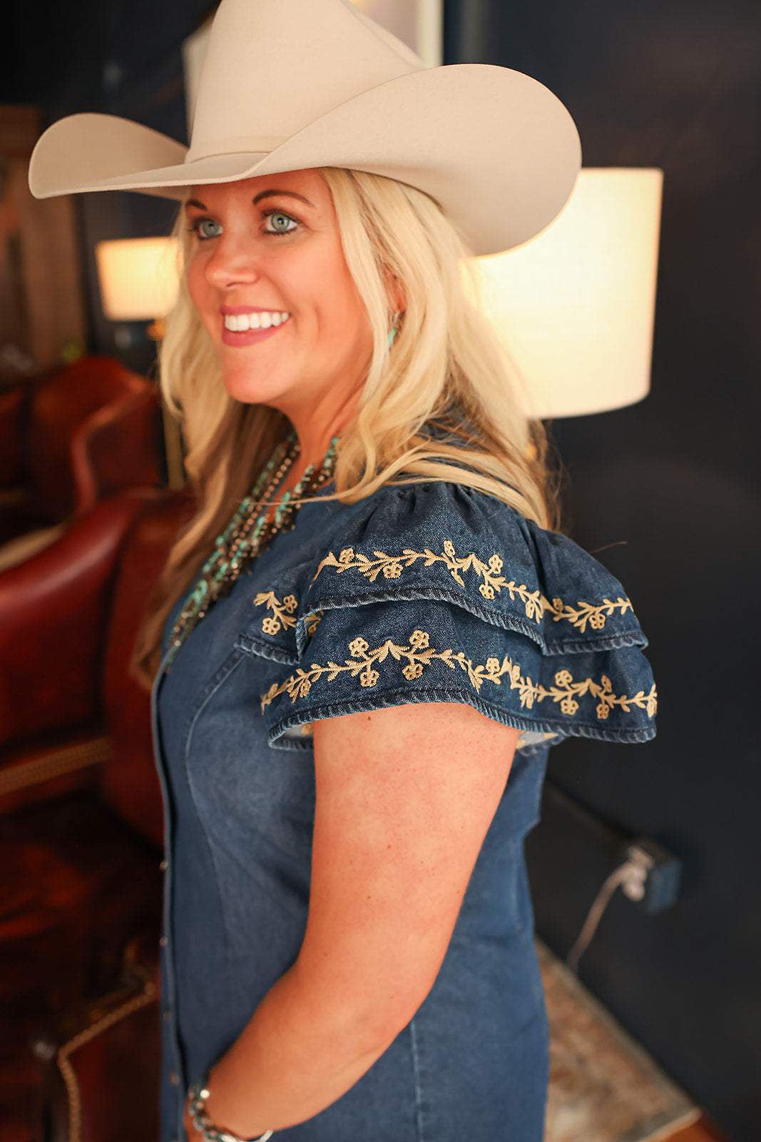 Woman with blonde hair standing in a side profile position wearing the Caylee Dress in a lifestyle scene. The focal point of this image is the ruffled sleeves with cream floral embroidery. 