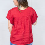 Woman with dark hair standing in a back profile position wearing the Chelsea Top against a white background. The focal point of this image is the fabric details and blue buck-stitch along cuff. The model paired this top with dark-wash denim shorts. 