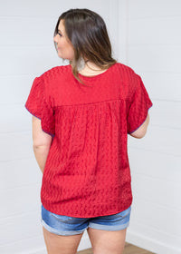 Woman with dark hair standing in a back profile position wearing the Chelsea Top against a white background. The focal point of this image is the fabric details and blue buck-stitch along cuff. The model paired this top with dark-wash denim shorts. 