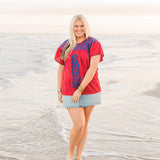 Woman with blonde hair standing in a front profile position wearing the Chelsea Top in a lifestyle scene. The focal point of this image is the top in its entirety. The model paired this top with a light-wash denim skirt. 