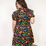 Woman with dark hair standing in a back profile stance against a white background wearing the Claire Dress. The focal point of the image is the graphics on back of dress and slight emphasis on belt. 