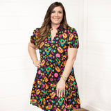 Woman with dark hair wearing the Claire Dress against a white background. The focal point of the image is the front graphics of the dress and slight emphasis on neckline and belt. 