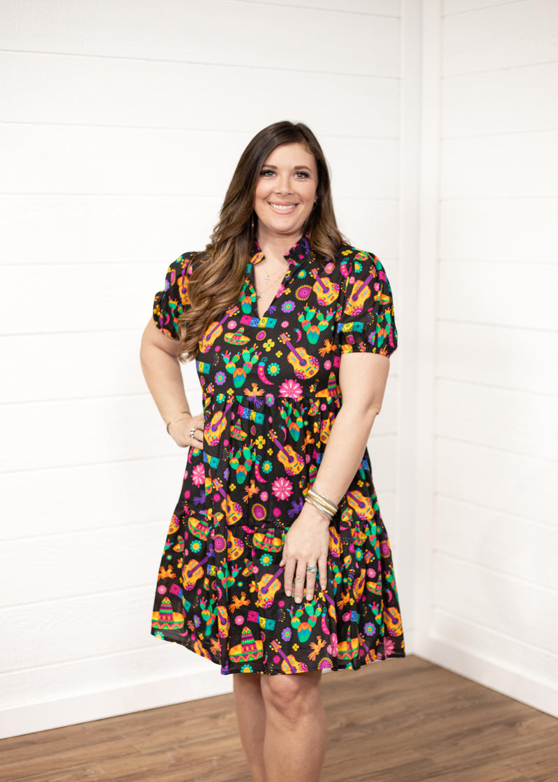 Woman with dark hair wearing the Claire Dress against a white background. The focal point of the image is the front graphics of the dress and slight emphasis on neckline and belt. 