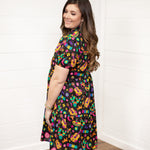 Woman with dark hair standing against a white background wearing the Claire Dress in a side profile position. The focal point of this image is the graphics on side of dress and slight emphasis on puffy sleeves. 