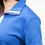 Woman with dark hair pictured at a side profile wearing the Daisy Top and Jane Bottoms set against a white background. The focal point of the image is the intricate detail of the fabric,  gold and white stripes on the cuff and collar as well as the quarter zip on the front.