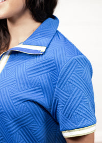 Woman with dark hair pictured at a side profile wearing the Daisy Top and Jane Bottoms set against a white background. The focal point of the image is the intricate detail of the fabric,  gold and white stripes on the cuff and collar as well as the quarter zip on the front.