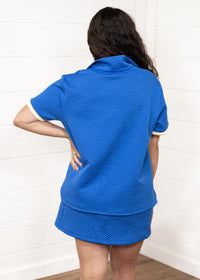 Woman with dark hair standing in a back profile position wearing the Daisy Top and Jane Bottoms set against a white background. The focal point of this image is the detailed grooves on the back of the top and bottoms. 