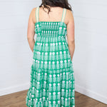 Woman with dark hair standing in a back profile position wearing the Demi Dress against a white background. The focal point of this image is graphics on back, yellow chevron straps as well as the scrunched stretched area on back. The model paired this dress with white moccasins. 