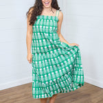 Woman with dark hair standing in a front profile position wearing the Demi Dress against a white background. The focal point of the image is the front graphics on dress as well as ruffle towards bottom. The model paired this dress with white moccasins. 