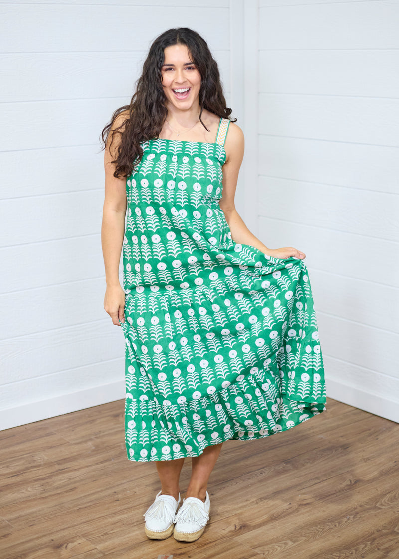 Woman with dark hair standing in a front profile position wearing the Demi Dress against a white background. The focal point of the image is the front graphics on dress as well as ruffle towards bottom. The model paired this dress with white moccasins. 