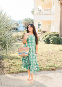 Woman with dark hair in a front profile position wearing the Demi Dress in a lifestyle scene. The focal point of this image is the dress in its entirety. The model paired this dress with white strappy heels and a woven hand-bag. 