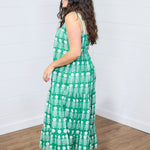 Woman with dark hair standing in a side profile position wearing the Demi Dress against a white background. The focal point of this image is the length of dress as well as graphics. The model paired this dress with white moccasins. 