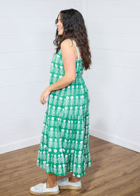 Woman with dark hair standing in a side profile position wearing the Demi Dress against a white background. The focal point of this image is the length of dress as well as graphics. The model paired this dress with white moccasins. 