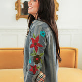 Woman with dark hair standing in a side profile position wearing the Diane Top in a lifestyle scene. The focal point of this image is the red, brown, green, and teal floral embroidery on sleeve. The model paired this top with mid-wash denim jeans. 