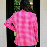 Woman with dark hair wearing a pink tweed blazer with gold buttons. Model paired blazer with dark-wash denim jeans. 