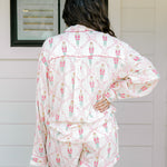 Woman with dark hair wearing a long-sleeve top and shorts pajama set featuring nutcracker graphics. 