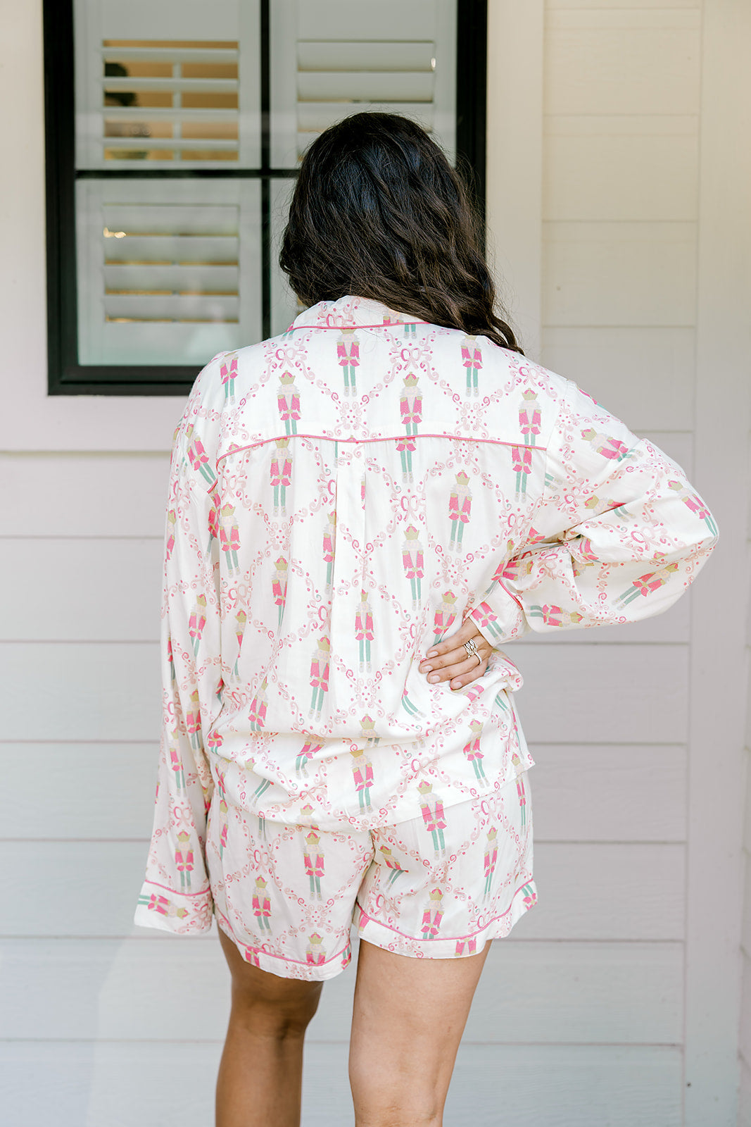Woman with dark hair wearing a long-sleeve top and shorts pajama set featuring nutcracker graphics. 