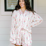 Woman with dark hair wearing a long-sleeve top and shorts pajama set featuring nutcracker graphics. 