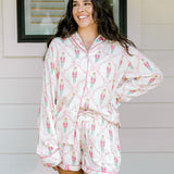 Woman with dark hair wearing a long-sleeve top and shorts pajama set featuring nutcracker graphics. 
