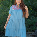 Woman with red hair standing in a front profile position wearing the Evie Dress in a lifestyle scene. The focal point of this image is the embroidery across chest, ruffles, v-neckline. 