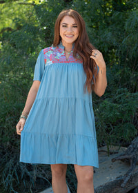 Woman with red hair standing in a front profile position wearing the Evie Dress in a lifestyle scene. The focal point of this image is the embroidery across chest, ruffles, v-neckline. 