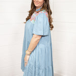 Woman with dark hair standing in a side profile position wearing the Evie Dress against a white background. The focal point of this image is the puffy sleeve with embroidery across shoulders. 