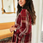Woman with dark hair standing in a side profile position wearing the Faye Top in a lifestyle scene. The focal point of this image is the ruffled sleeve long sleeve as well as the length of top. The model paired this top with light-wash denim jeans. 