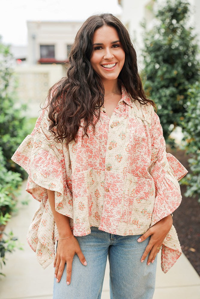 Woman with dark hair wearing a poncho style top with floral patchwork and light-wash denim jeans. 
