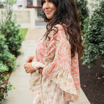 Woman with dark hair wearing a poncho style top with floral patchwork and light-wash denim jeans. 
