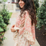 Woman with dark hair wearing a poncho style top with floral patchwork and light-wash denim jeans. 