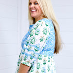 Woman with blonde hair standing in a side profile position wearing the Helen Dress against a white background. The focal point for this image is the up-close view of embroidery on quarter sleeve and pleated cuff. 