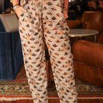 Woman with dark hair wearing the Jane Pant in tan with multicolored cowboy hats, and brown cowboy boots.