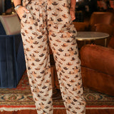 Woman with dark hair wearing the Jane Pant in tan with multicolored cowboy hats, and brown cowboy boots.